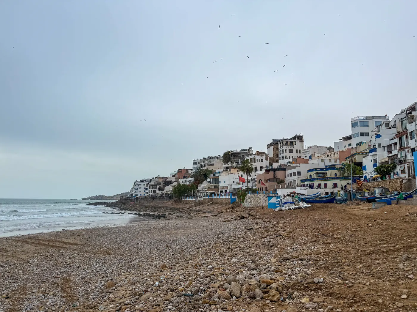 Rocky shoreline, fishing boats and village buildings on the Taghazout coast.