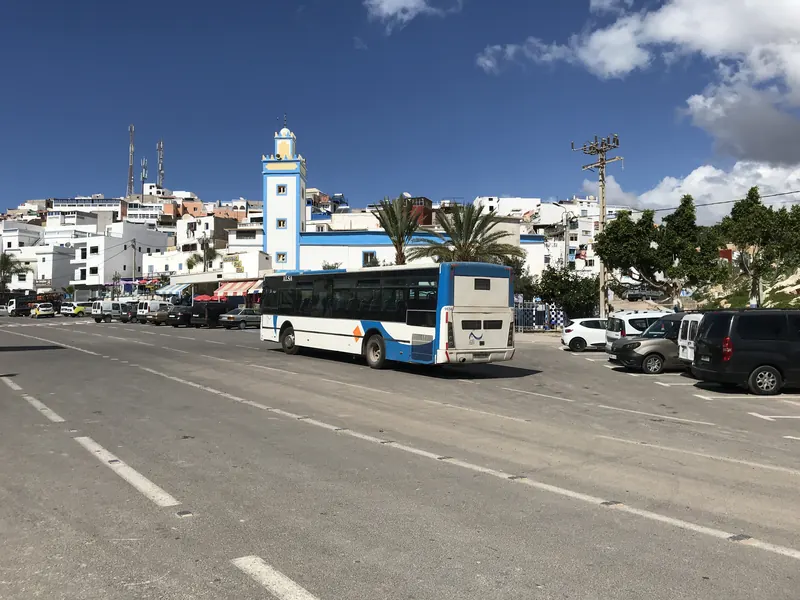 An ALSA bus on a street in Taghazout, with a blue-and-white mosque behind it.