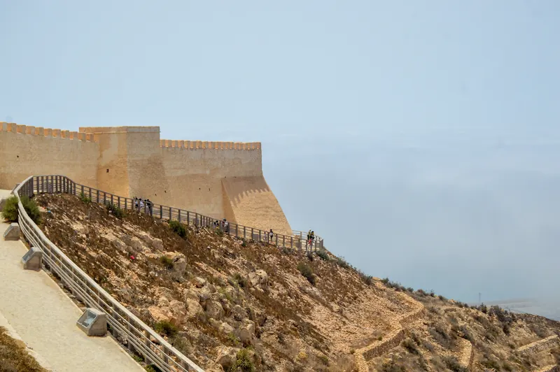 A visitor walkway beside the reconstructed wall of Agadir Oufella Kasbah on the hillside.