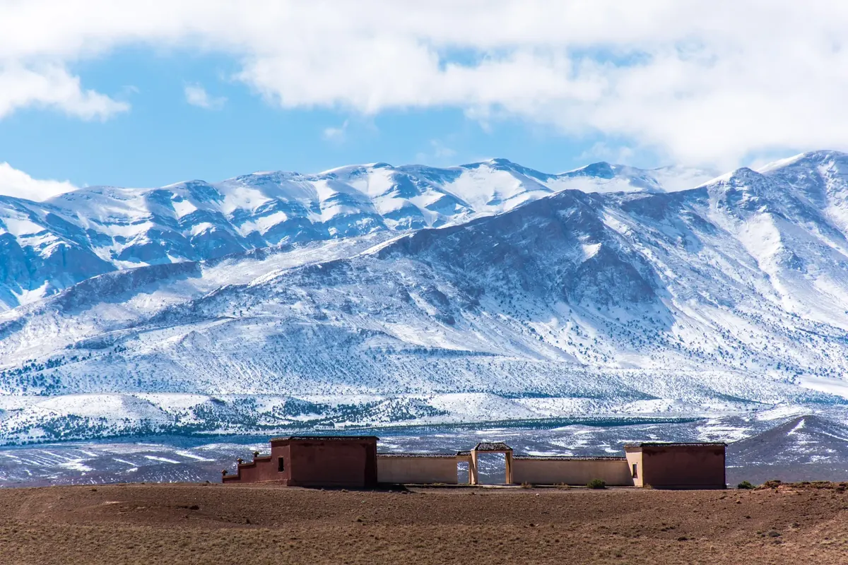Snowy High Atlas mountains and a rural roadside settlement between Midelt and Fès, Morocco.