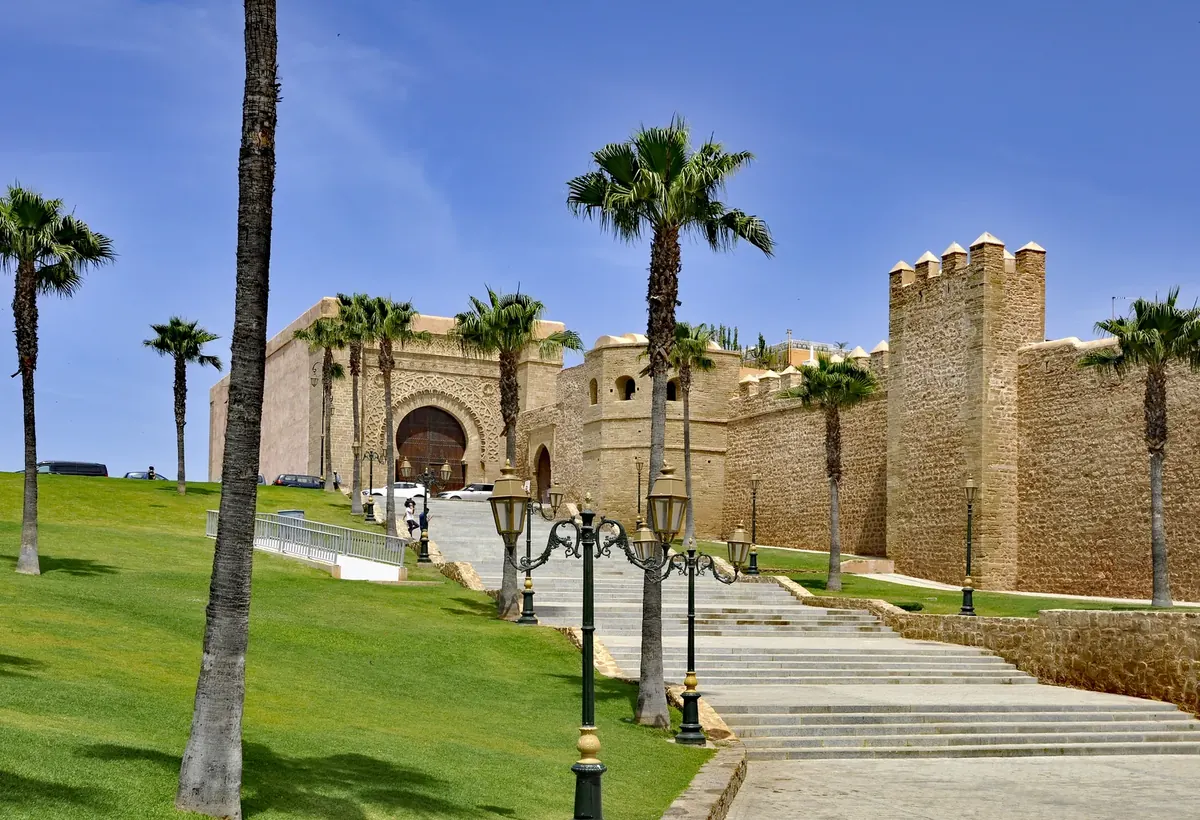 Stone gate and fortification walls at the Kasbah of the Udayas in Rabat, with palm trees and a walkway