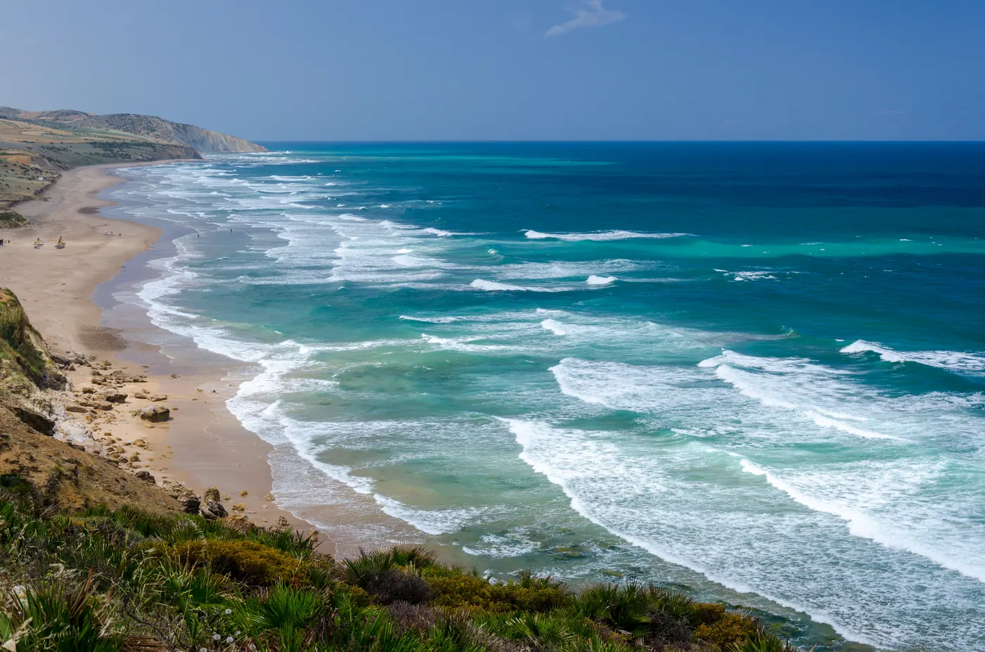 Wide view of the sandy Atlantic coastline at Paradise Beach near Asilah, Morocco, with waves below coastal cliffs.