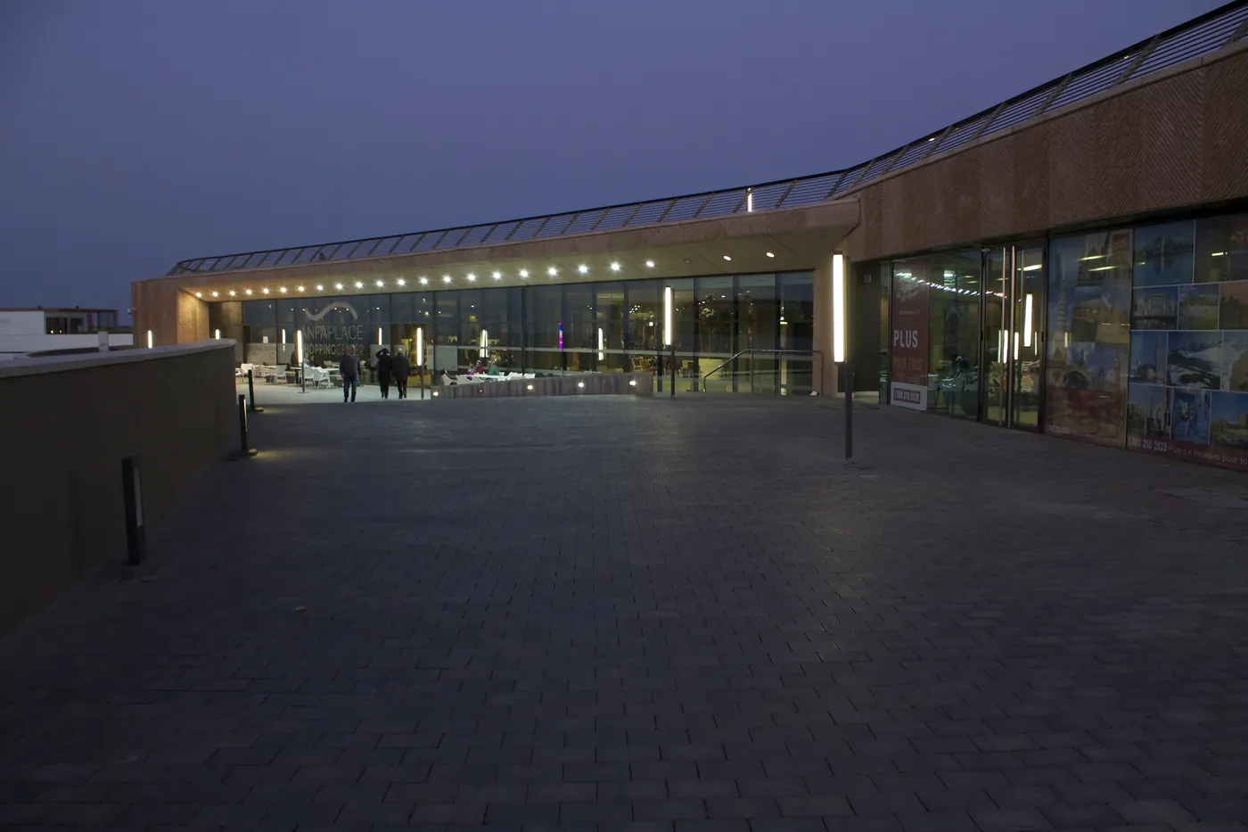 Archival after-dark view of a lit public commercial-complex entrance in Casablanca, with pedestrians on a paved forecourt.