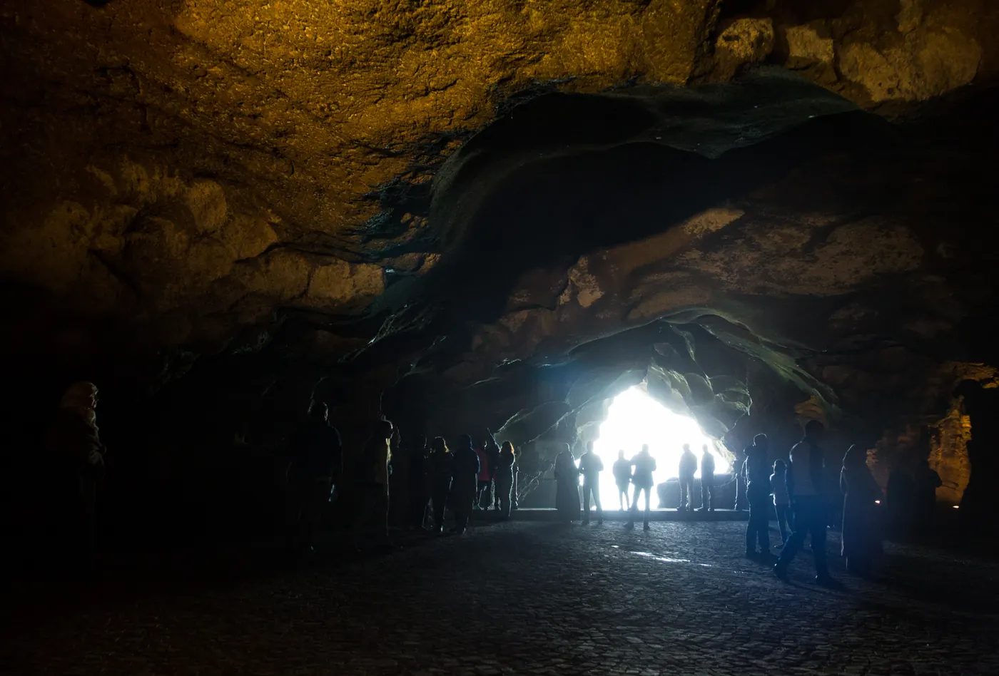 Visitors silhouetted inside the Caves of Hercules looking toward the bright ocean opening