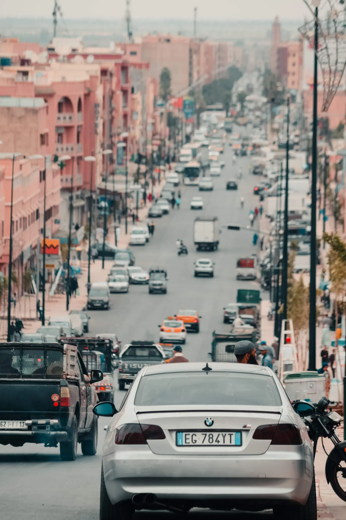 Cars, motorbikes and pedestrians on a broad urban street in Morocco, viewed from above.