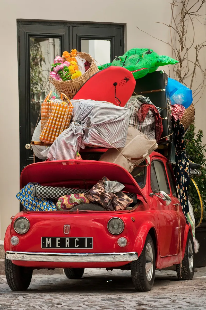 A classic red Fiat overloaded with bags and household items in Paris.