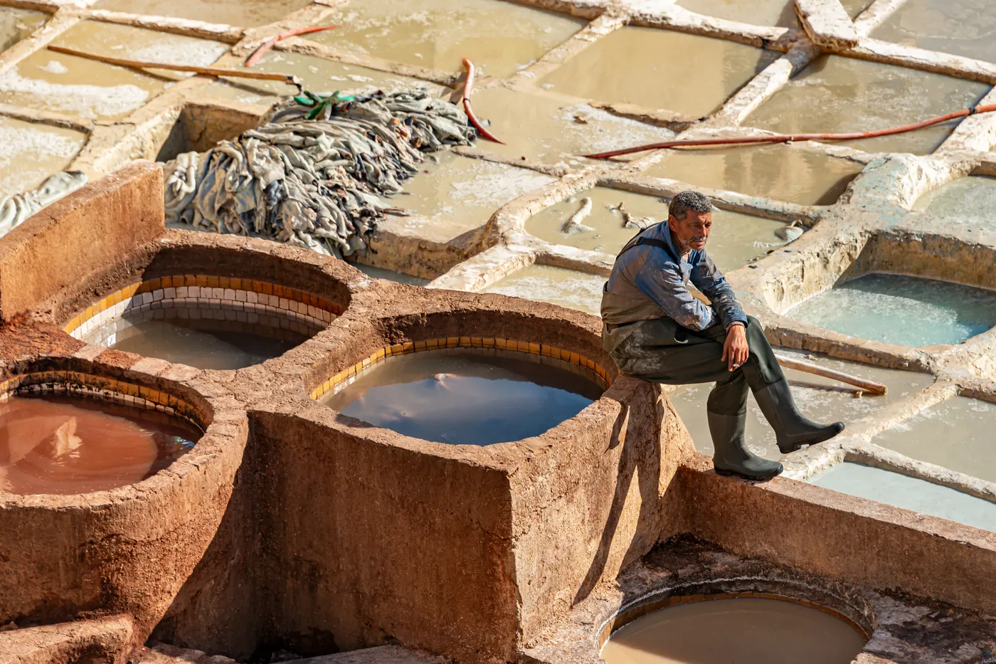 A worker seated among circular tanning vats at Chouara Tannery in Fes, Morocco.