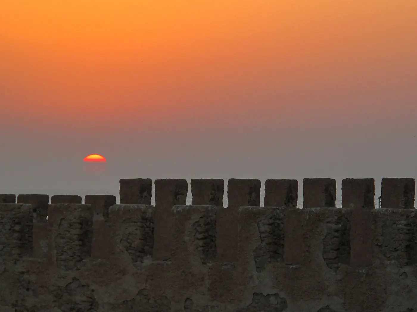 Sun setting behind the stone crenellations of Essaouira ramparts.