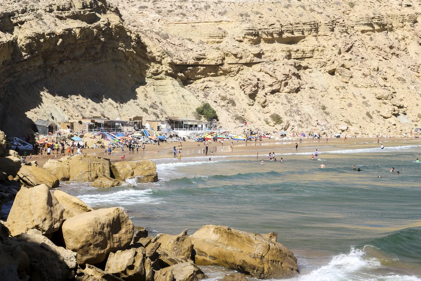 People along Imsouane Beach beneath the rocky cliffs of Imsouane Bay in Morocco.