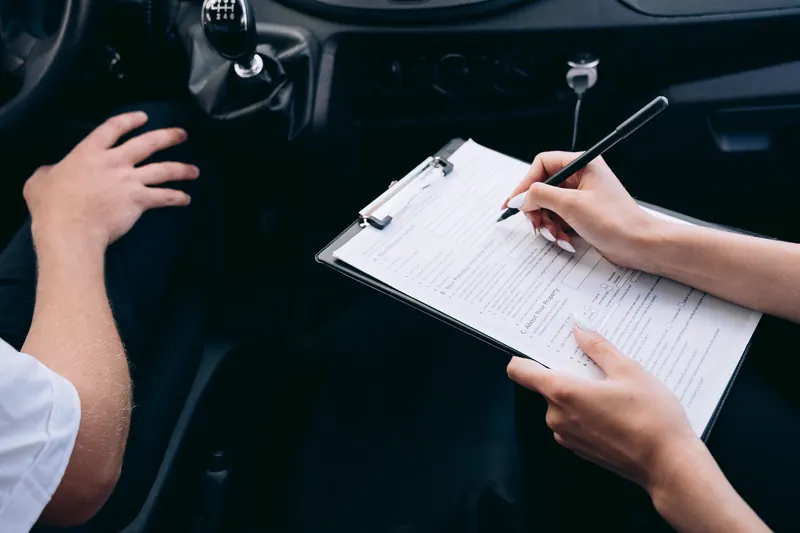 Hands filling in a clipboard beside the gear selector inside a car.