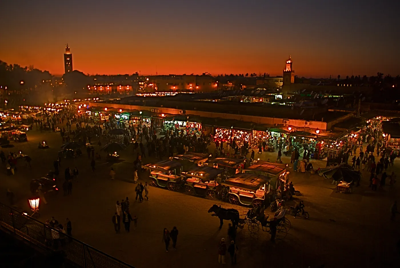 Evening view across Jemaa el-Fna square in Marrakech, with market stalls and the Koutoubia minaret.