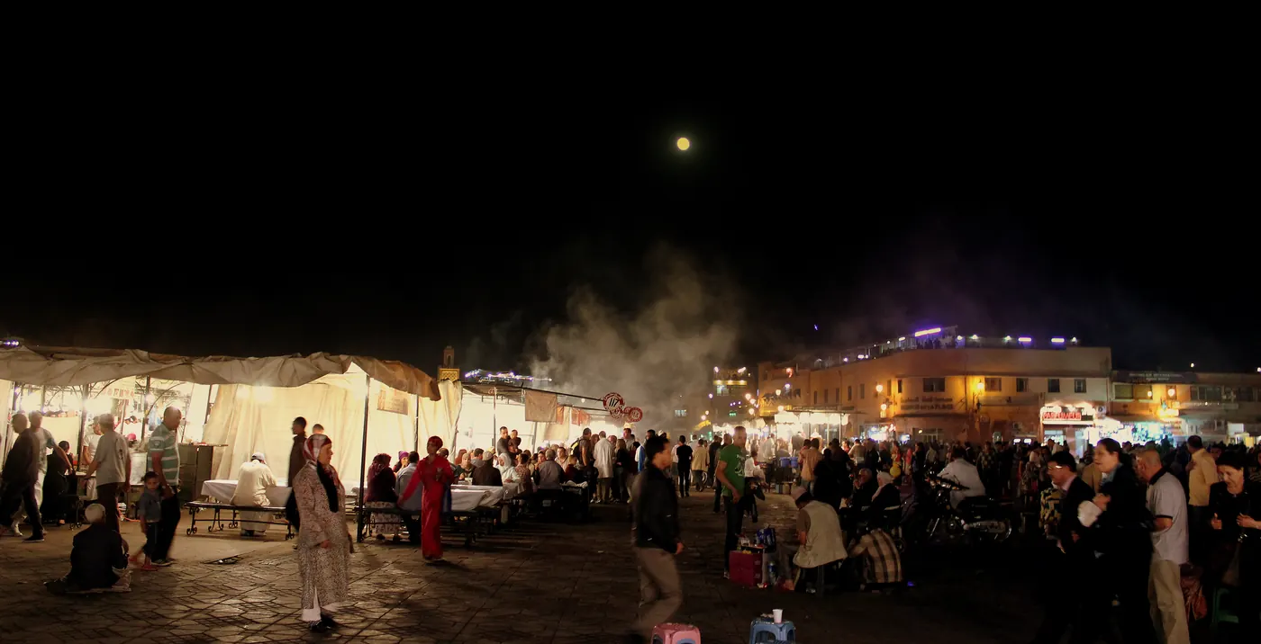 Night scene at Jemaa el-Fna in Marrakech in 2013, with bright food stalls, smoke, pedestrians and people gathered in the square.