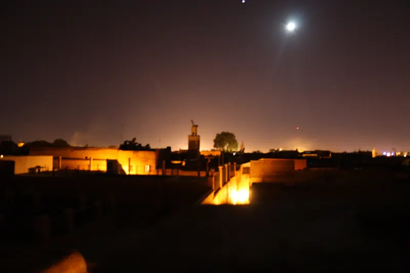 Moonlit night sky above low Marrakech rooftops and distant city lights.
