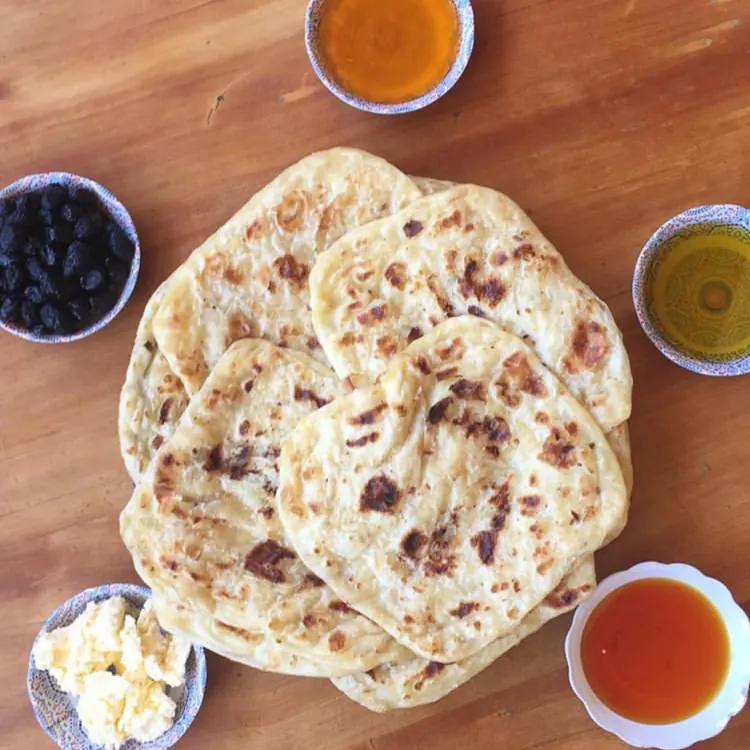 Msemen flatbreads with honey, olive oil, butter and olives on a wooden table.