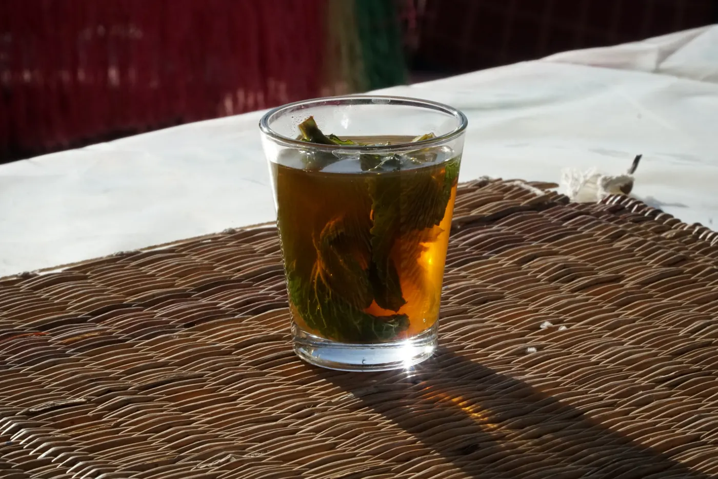 A glass of mint tea with fresh mint leaves on a woven mat in Marrakesh.