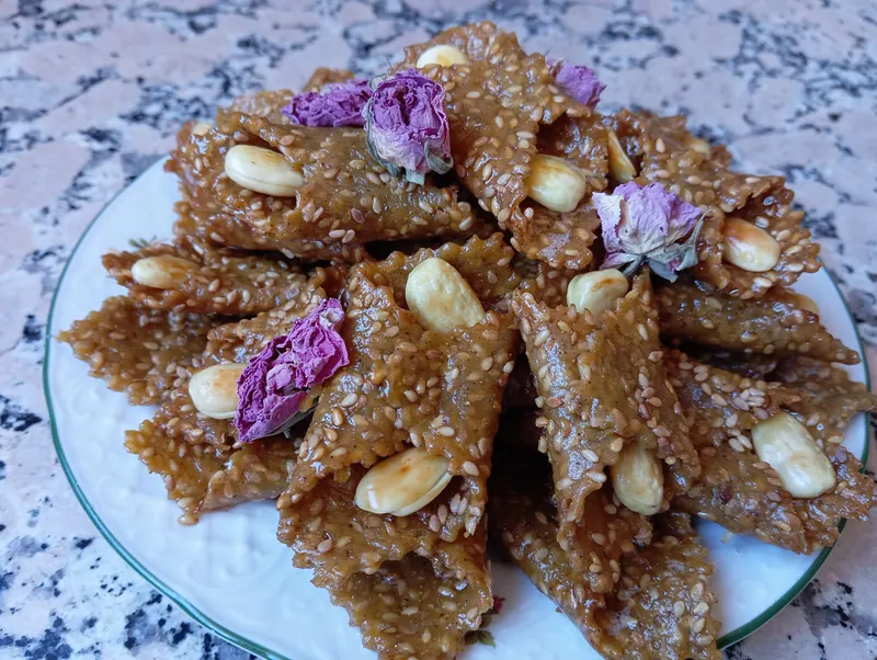 Plate of Beligha pastries with sesame, whole almonds and dried rose buds