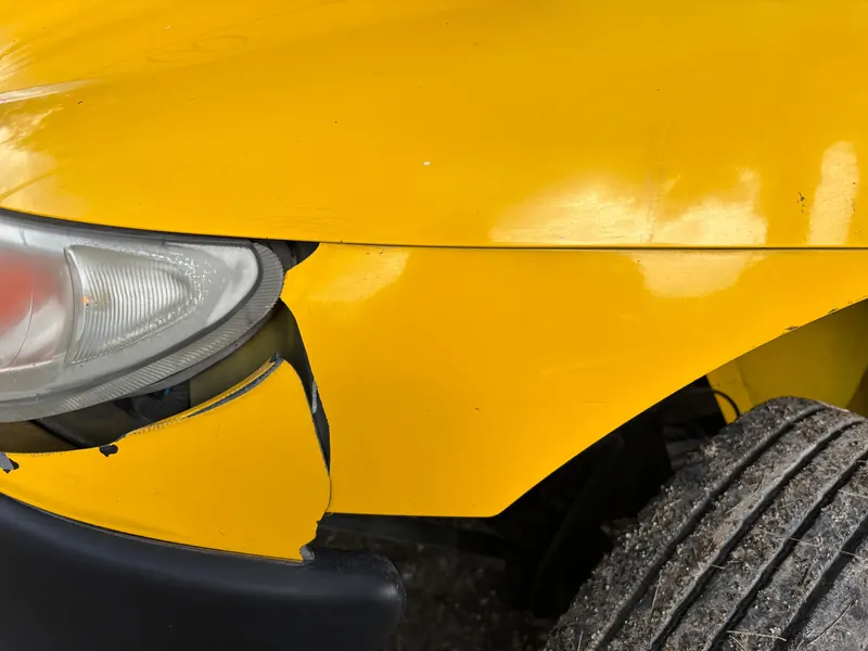 Close-up of a damaged yellow car bumper and headlight; generic stock image.