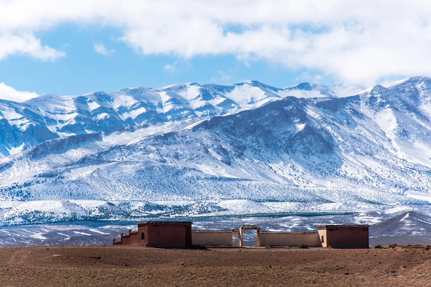 Snow-covered High Atlas ridges above a roadside building on the Midelt to Fès route in Morocco.