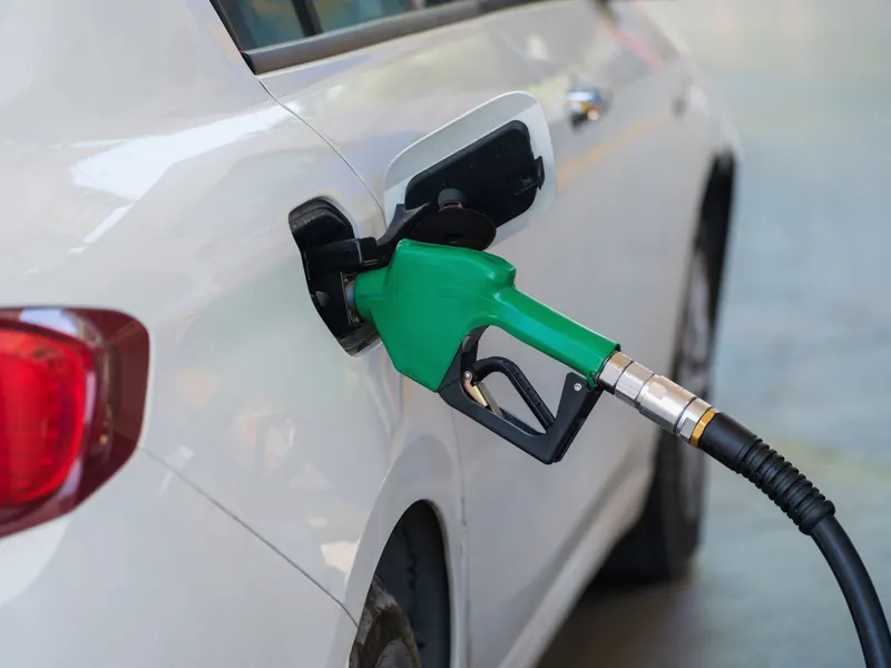 Green fuel nozzle refuelling a white car at a generic fuel station