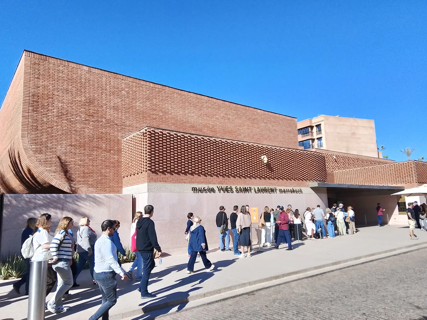 Exterior of the Musée Yves Saint Laurent Marrakech, showing the brick façade and visitors waiting at the entrance.