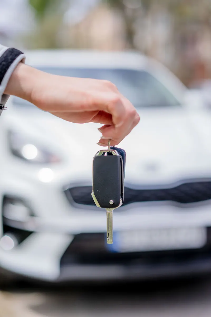 A hand holding a car key in front of a white vehicle outdoors.