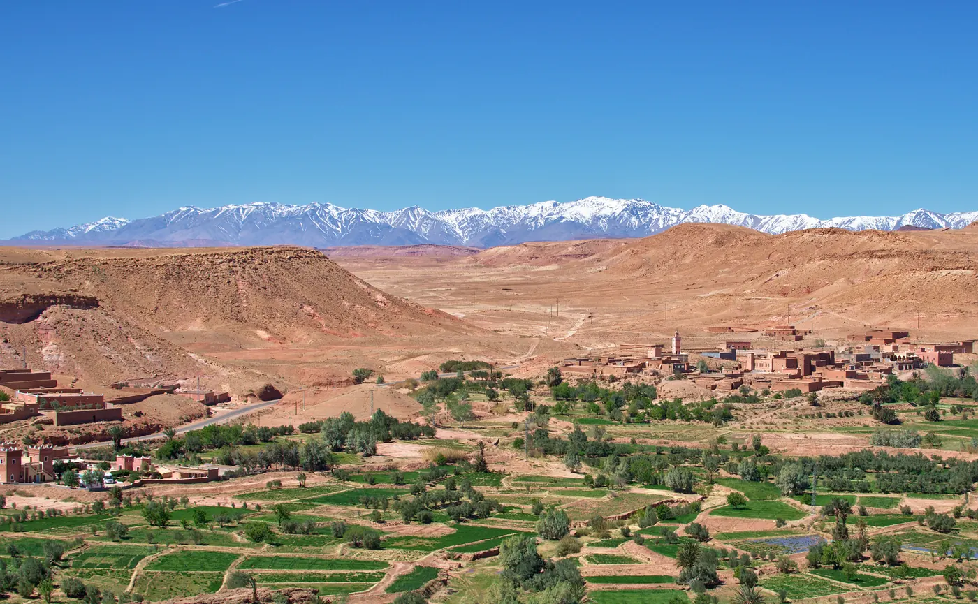 Wide view of Aït Benhaddou in Morocco with earthen buildings, palms and dry hills.