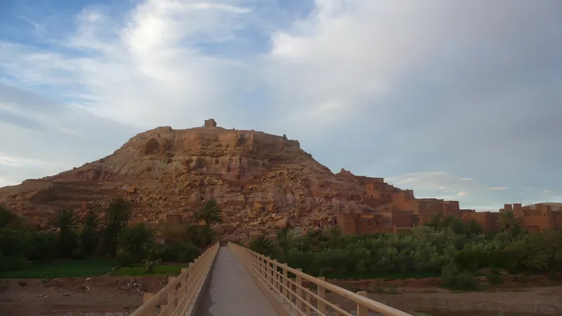 Pedestrian bridge leading toward the Ksar of Aït Benhaddou before sunset.