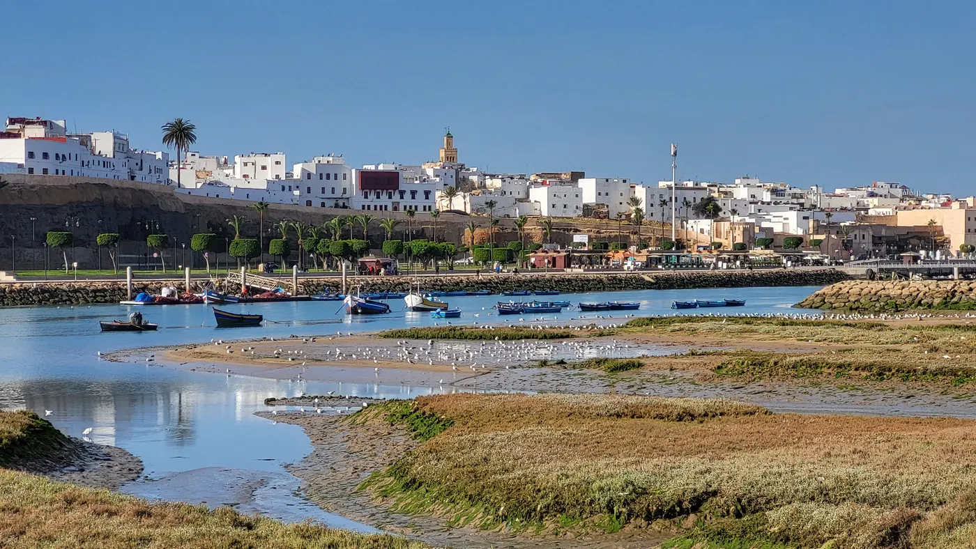 Boats on the Bouregreg river with Rabat's waterfront and white buildings across the water.