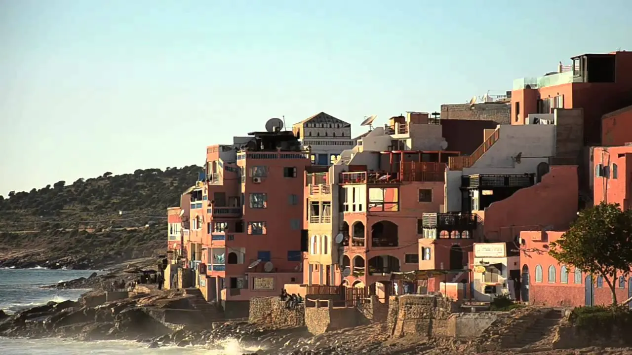 Sunlit buildings along the rocky shore at Taghazout, Morocco, seen from the beach.