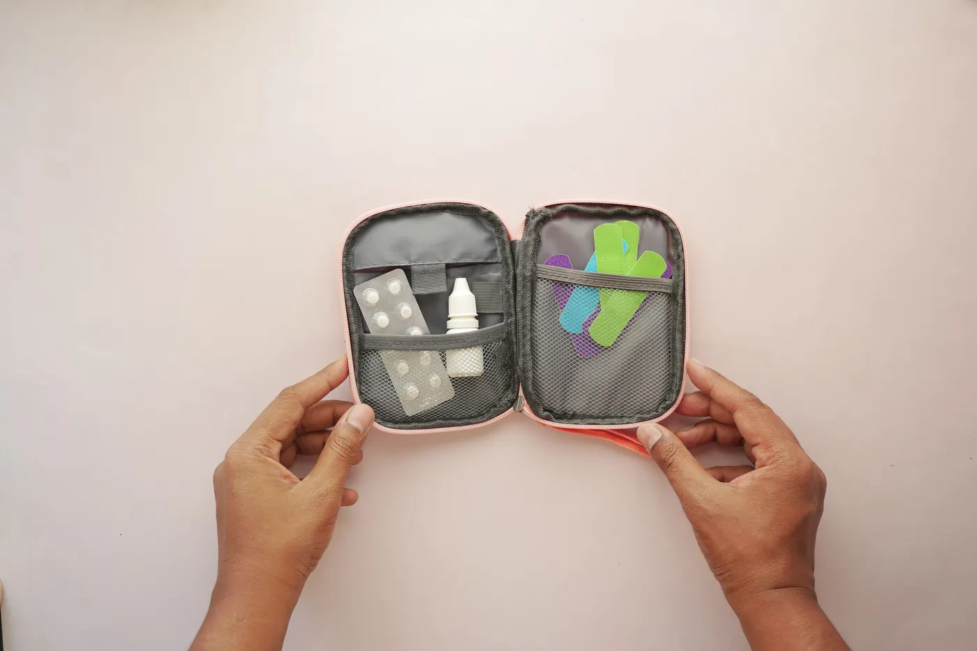 Hands holding an open first-aid kit with tablets and bandages
