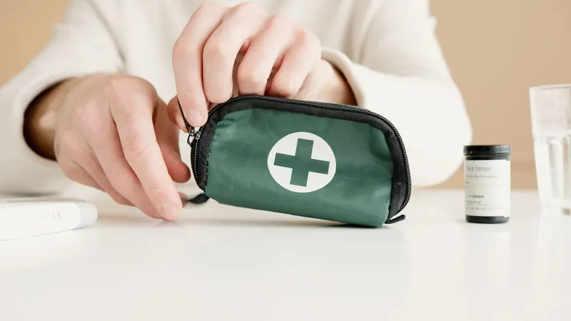 Hands holding a black and green first-aid pouch beside medical test strips