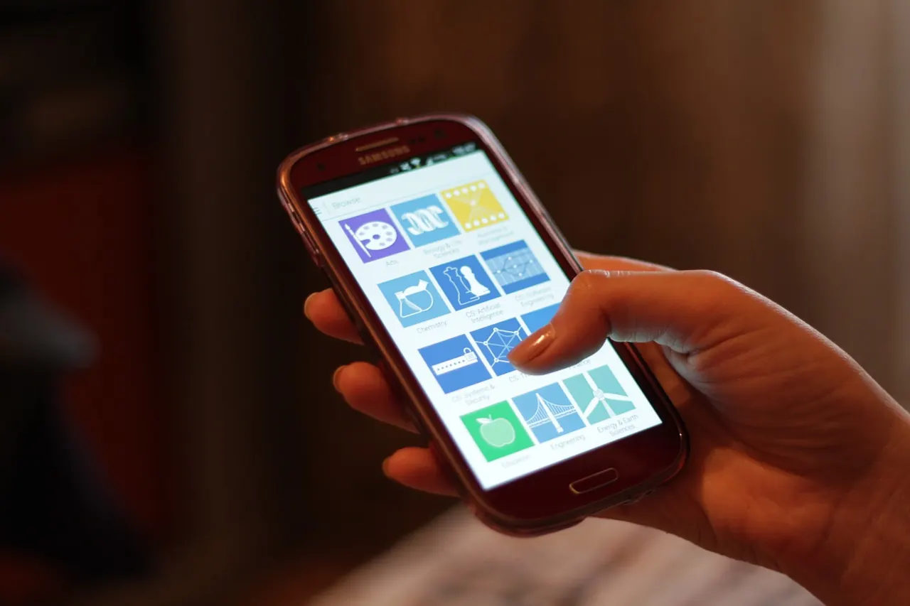 A hand holding an Android smartphone with its home screen visible