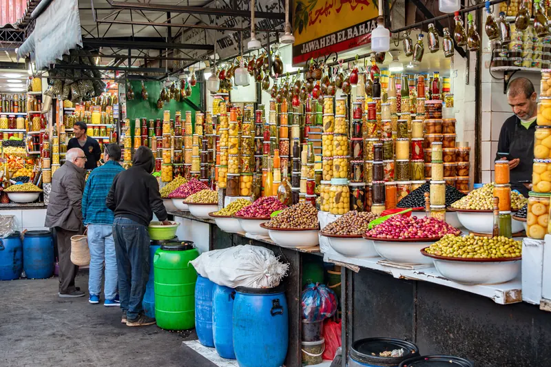 Shoppers beside bowls of olives and jars of preserved foods in a Marrakech souk.