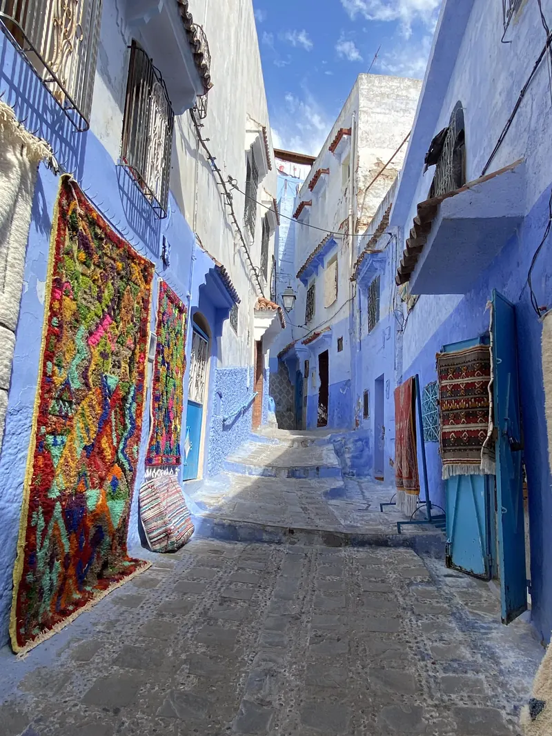 Blue-painted, narrow lane with steps and rugs in Chefchaouen’s medina