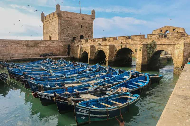 Blue fishing boats beside the stone citadel at Essaouira port on Morocco’s Atlantic coast