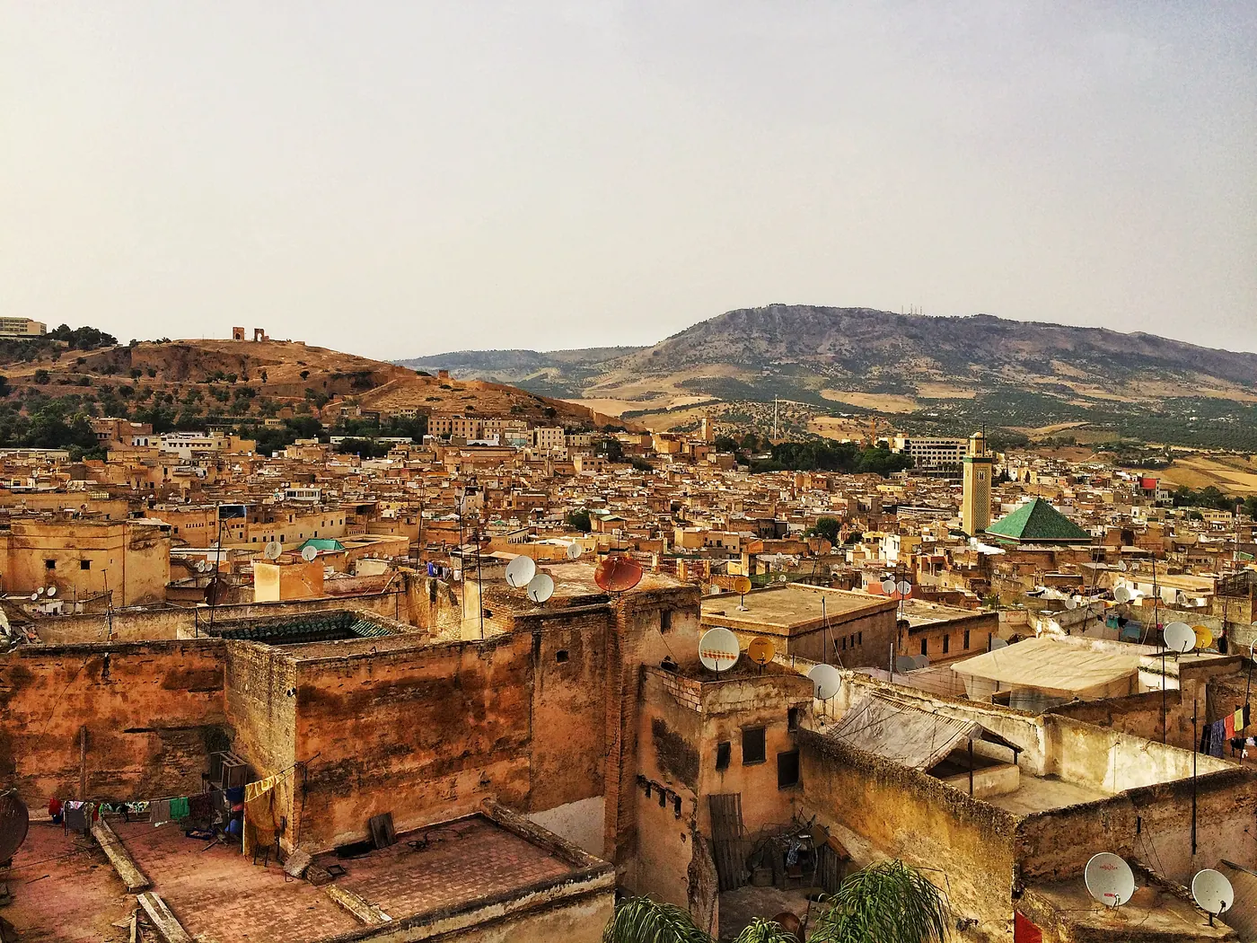 Wide view over the rooftops and minaret of the Medina of Fez, with hills in the background