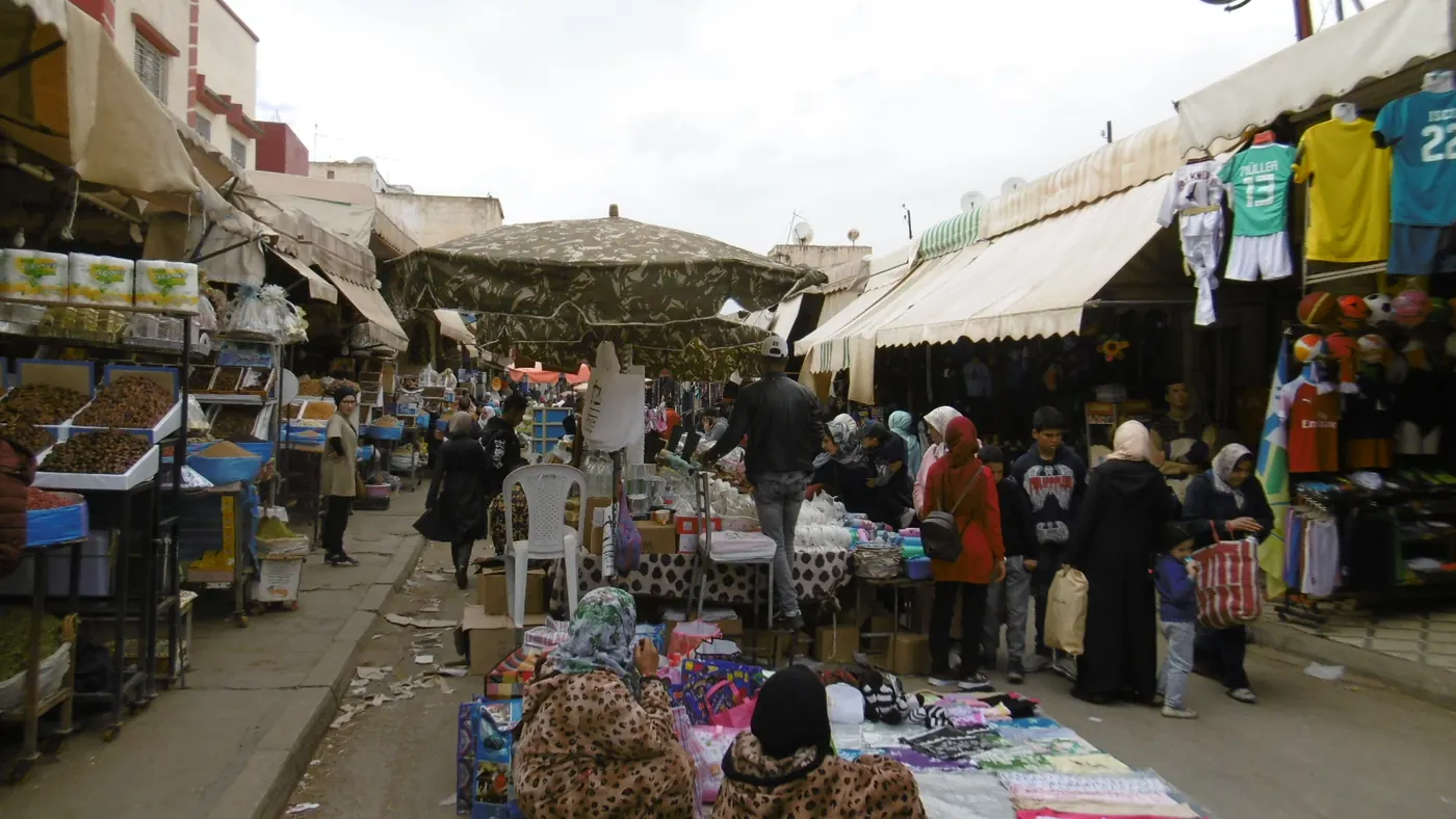 Shoppers and market stalls along a covered lane in the Medina of Meknes.