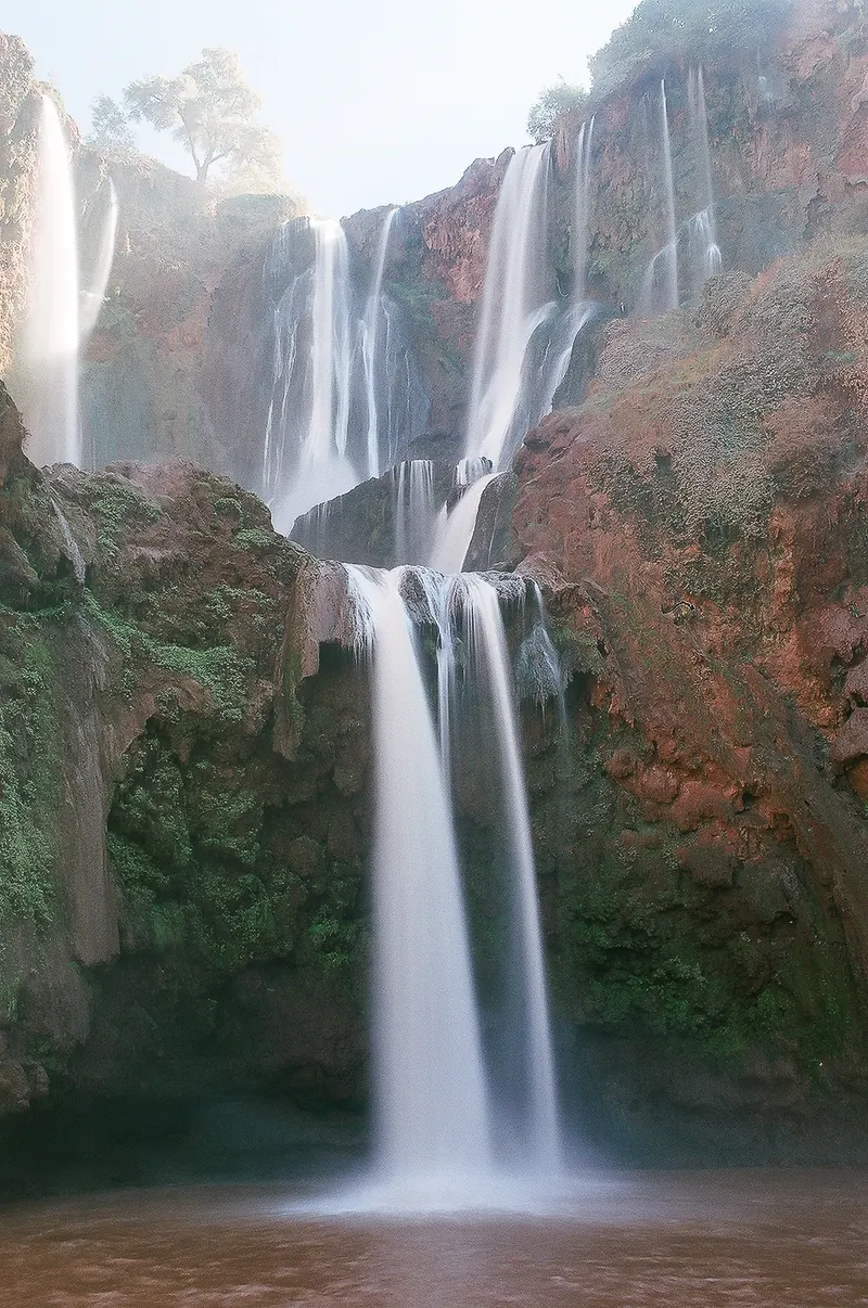 Vertical view of Ouzoud Falls spilling down tiered reddish cliffs.