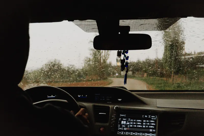 Raindrops on a car windscreen while driving along a rainy rural road.